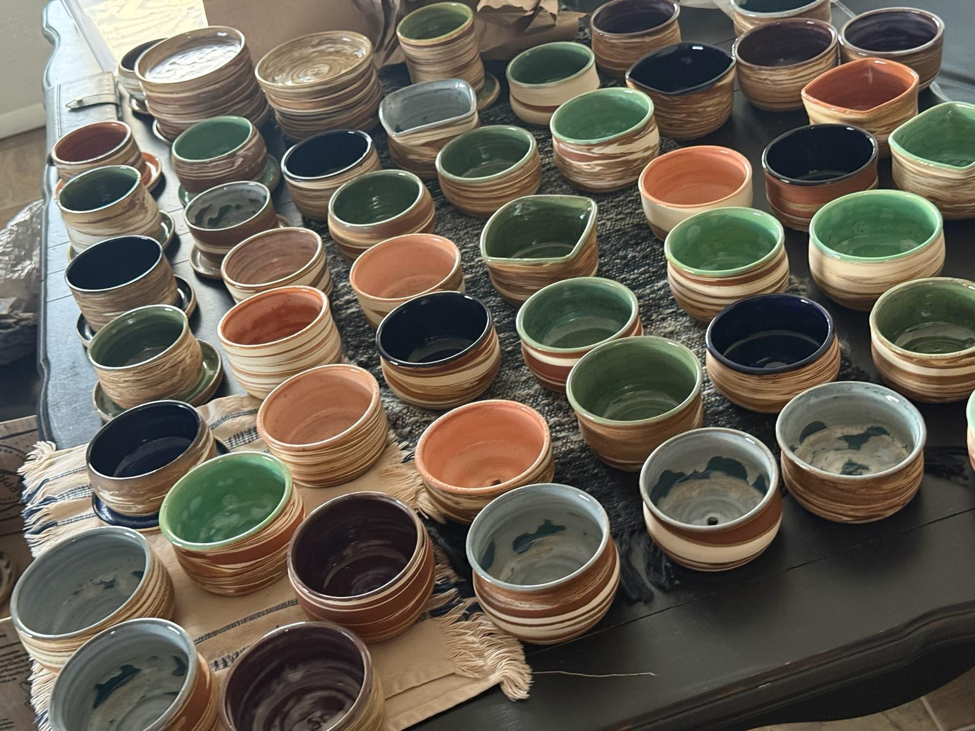 Dozens of Taya's handmade swirled clay pots with green, blue, black and terracotta glazed interiors spread across a table