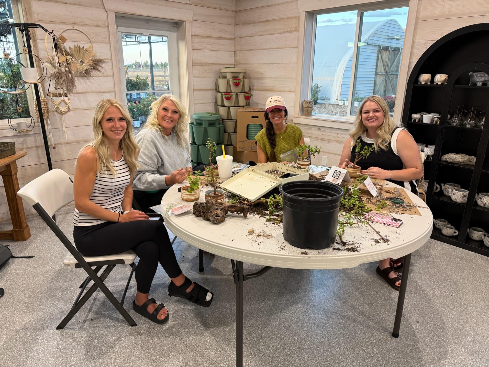 Four participants sit around a round workshop table with soil, tools and a black nursery pot in a bright studio